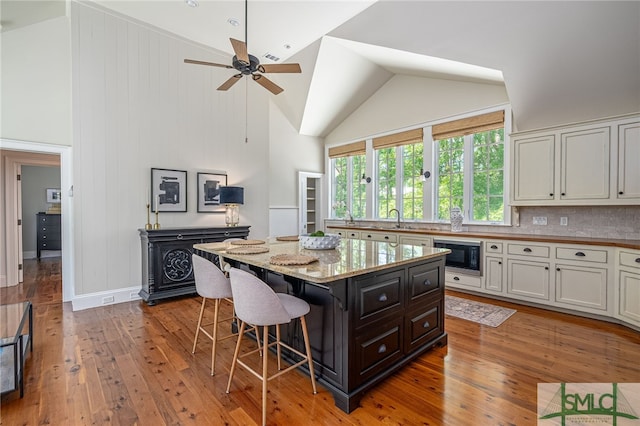 kitchen with ceiling fan, a center island, tasteful backsplash, black microwave, and light hardwood / wood-style flooring