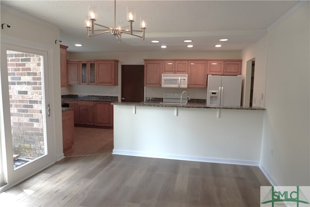 kitchen with a notable chandelier, white appliances, light wood-type flooring, a breakfast bar area, and dark stone counters