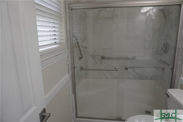 bathroom featuring a shower with door and toilet