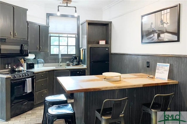 kitchen with a kitchen breakfast bar, crown molding, butcher block countertops, black appliances, and sink