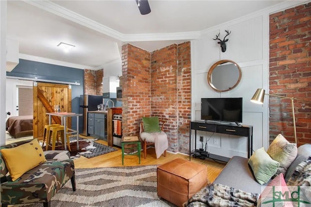 living room featuring ceiling fan, crown molding, wood-type flooring, a barn door, and brick wall