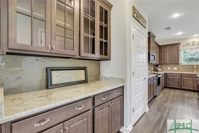 kitchen with dark brown cabinetry, light wood-type flooring, stainless steel appliances, light stone countertops, and decorative backsplash