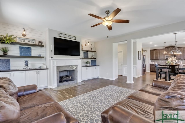 living room featuring ceiling fan with notable chandelier, a tiled fireplace, and dark hardwood / wood-style flooring