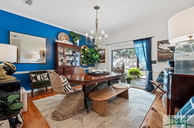 dining area with hardwood / wood-style floors, a notable chandelier, ornamental molding, and a textured ceiling