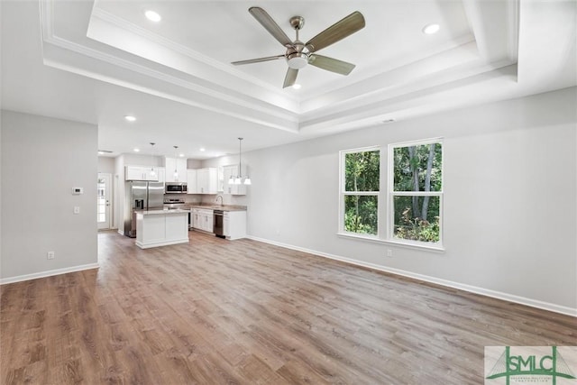 unfurnished living room with sink, light hardwood / wood-style flooring, ceiling fan, a tray ceiling, and ornamental molding