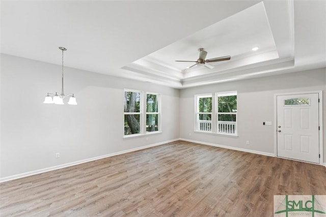 unfurnished living room with crown molding, ceiling fan with notable chandelier, light hardwood / wood-style flooring, and a tray ceiling