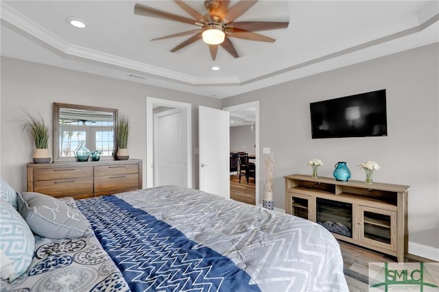 bedroom with crown molding, a raised ceiling, ceiling fan, and light wood-type flooring