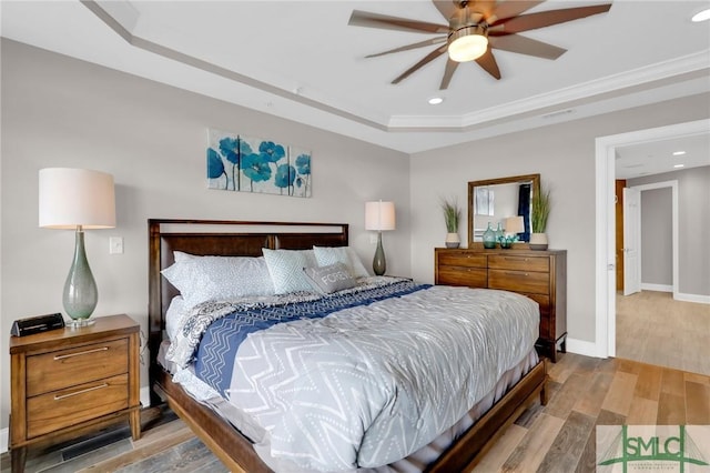 bedroom with ceiling fan, ornamental molding, wood-type flooring, and a tray ceiling