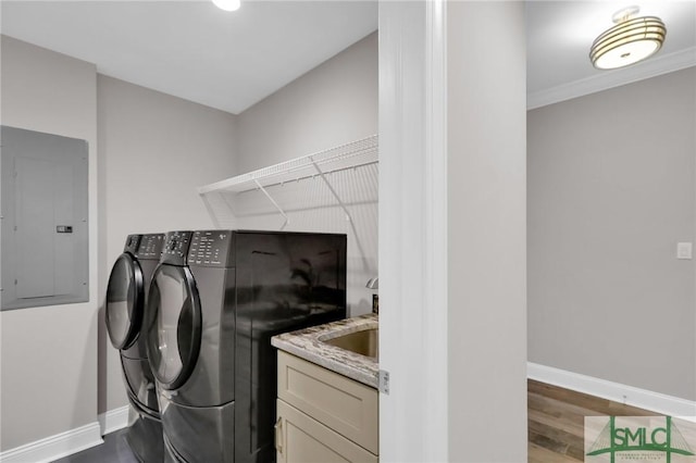 clothes washing area with wood-type flooring, sink, ornamental molding, electric panel, and washer and clothes dryer