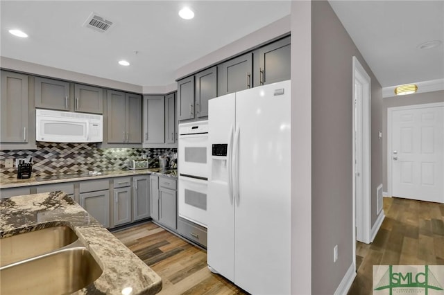 kitchen with gray cabinets, backsplash, light stone counters, light hardwood / wood-style floors, and white appliances