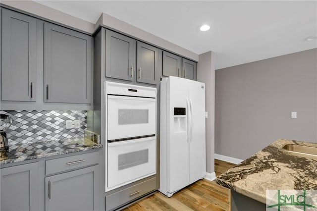 kitchen featuring white appliances, gray cabinets, decorative backsplash, and stone counters