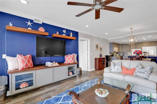 living room featuring ornamental molding, ceiling fan with notable chandelier, and light wood-type flooring