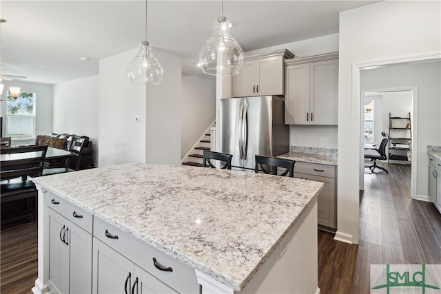 kitchen featuring ceiling fan, a kitchen island, stainless steel refrigerator, dark wood-type flooring, and pendant lighting