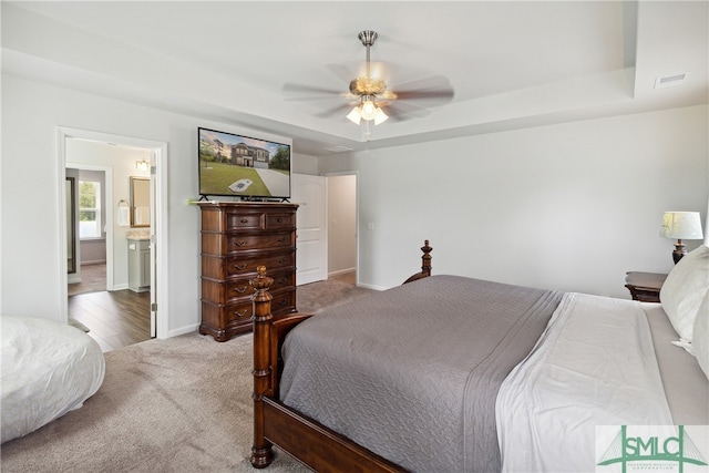 bedroom with ceiling fan, a tray ceiling, ensuite bathroom, and carpet floors