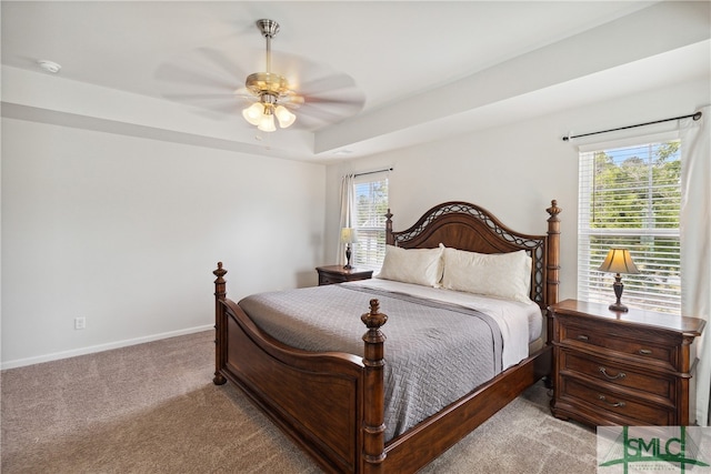 carpeted bedroom featuring ceiling fan, a raised ceiling, and multiple windows