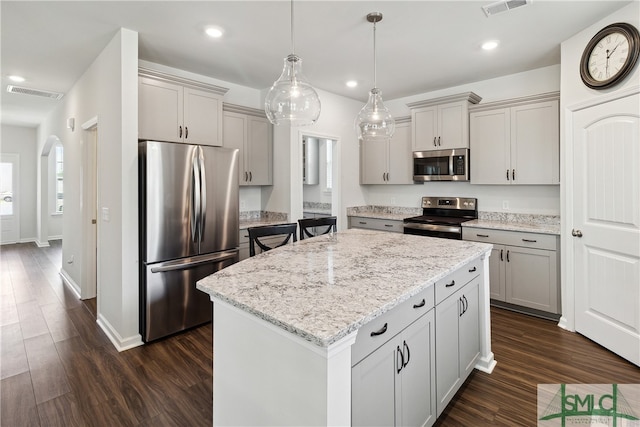 kitchen with a center island, decorative light fixtures, dark hardwood / wood-style floors, appliances with stainless steel finishes, and light stone counters