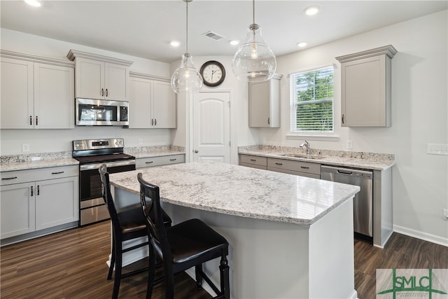 kitchen with decorative light fixtures, dark hardwood / wood-style flooring, stainless steel appliances, sink, and a kitchen island