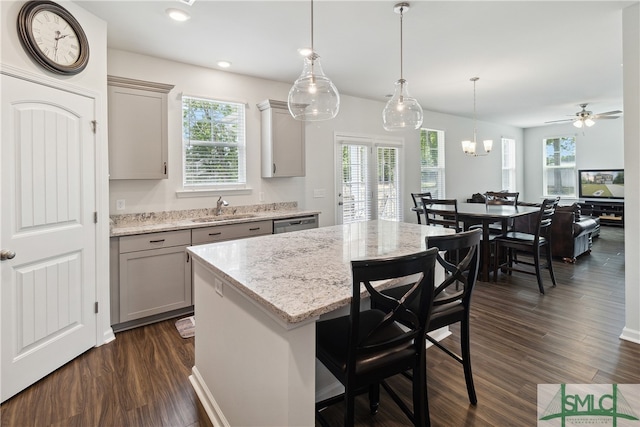 kitchen with hanging light fixtures, ceiling fan with notable chandelier, dark hardwood / wood-style flooring, sink, and a kitchen island