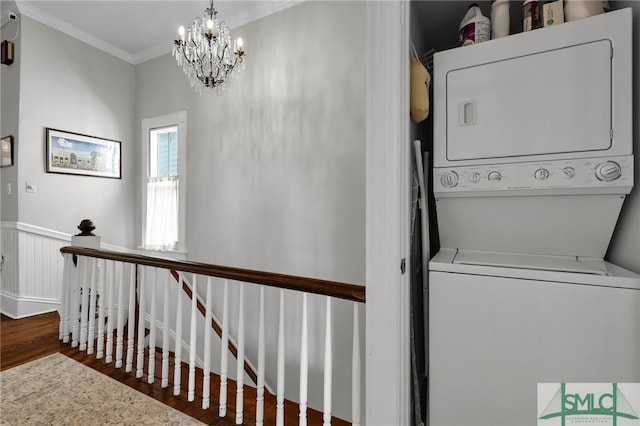 clothes washing area featuring a chandelier, ornamental molding, wood-type flooring, and stacked washer / drying machine