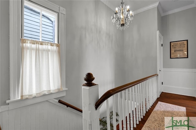 stairs with ornamental molding, wood-type flooring, and a notable chandelier