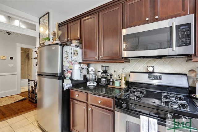 kitchen featuring tasteful backsplash, dark stone counters, stainless steel appliances, and light wood-type flooring