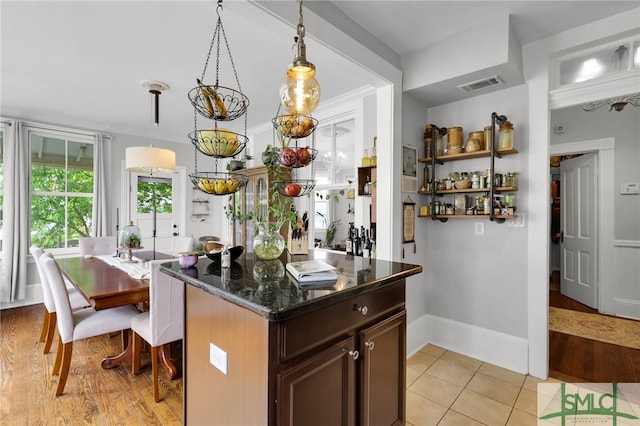 kitchen featuring crown molding, dark stone counters, decorative light fixtures, and light tile floors