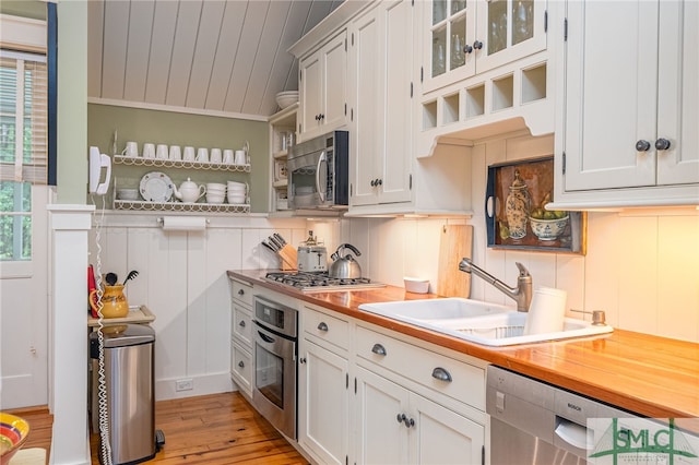 kitchen featuring appliances with stainless steel finishes, vaulted ceiling, white cabinetry, sink, and light wood-type flooring