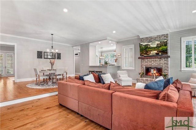 living room featuring ornamental molding, light hardwood / wood-style flooring, a brick fireplace, and a notable chandelier