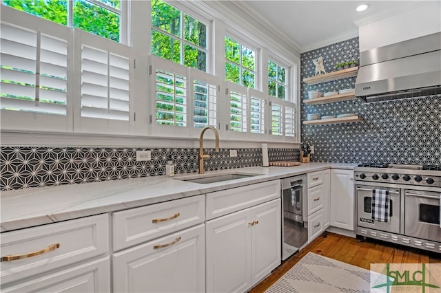 kitchen featuring wall chimney exhaust hood, light hardwood / wood-style flooring, white cabinetry, double oven range, and sink