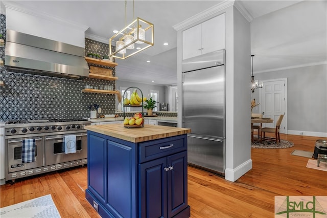 kitchen with high end appliances, light hardwood / wood-style floors, wall chimney range hood, and blue cabinetry