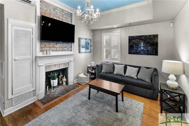 living room featuring wood-type flooring, a fireplace, a tray ceiling, and an inviting chandelier