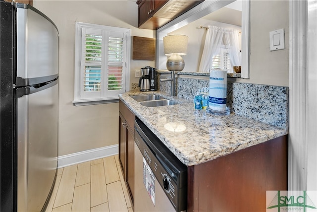 kitchen with appliances with stainless steel finishes, dark brown cabinetry, sink, and light stone countertops