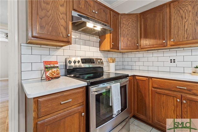 kitchen featuring decorative backsplash, stainless steel electric range oven, crown molding, and light tile patterned flooring