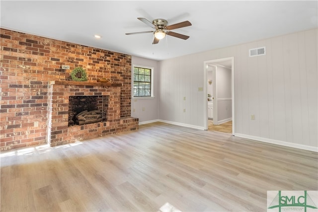 unfurnished living room with ceiling fan, a fireplace, brick wall, and light hardwood / wood-style flooring