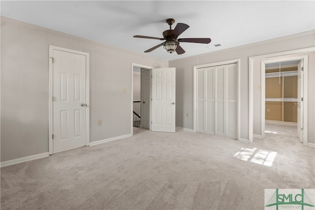 unfurnished bedroom featuring ceiling fan, ornamental molding, light carpet, and multiple closets