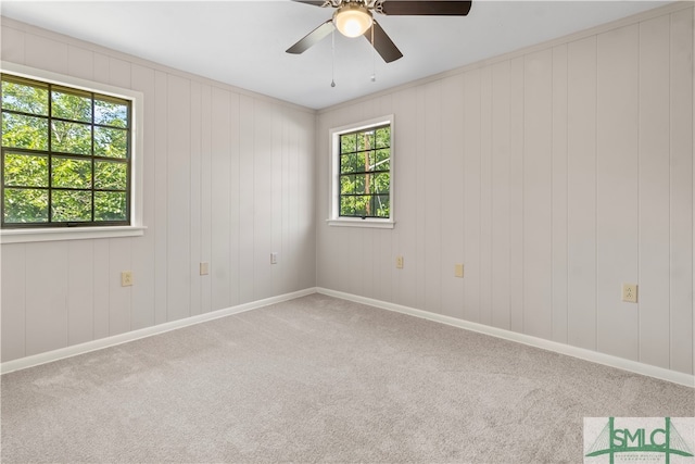 carpeted spare room with wood walls, plenty of natural light, and ceiling fan