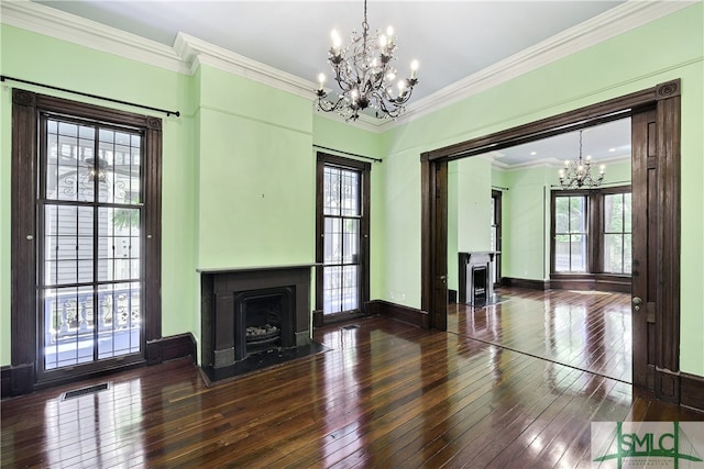 unfurnished living room featuring a healthy amount of sunlight, dark hardwood / wood-style floors, an inviting chandelier, and ornamental molding