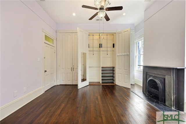 unfurnished living room with ceiling fan, a wood stove, and dark wood-type flooring