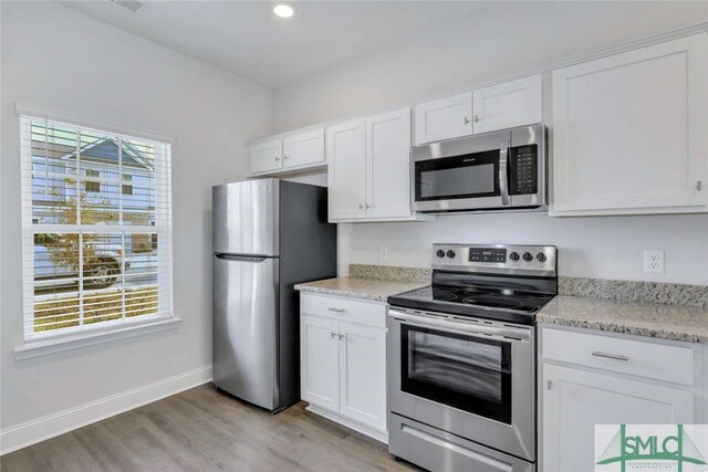 kitchen with stainless steel appliances, a healthy amount of sunlight, white cabinets, and light wood-type flooring