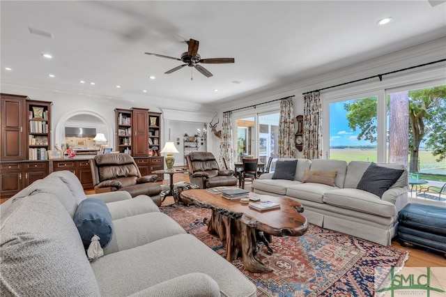 living room featuring a healthy amount of sunlight, ceiling fan, light wood-type flooring, and crown molding