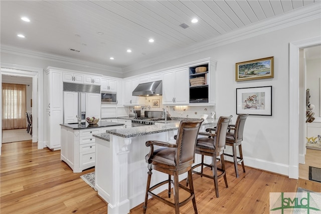 kitchen with light hardwood / wood-style floors, white cabinets, built in appliances, and wall chimney exhaust hood