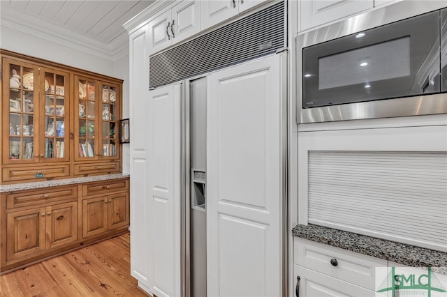 kitchen with light stone counters, light hardwood / wood-style flooring, crown molding, built in appliances, and white cabinetry