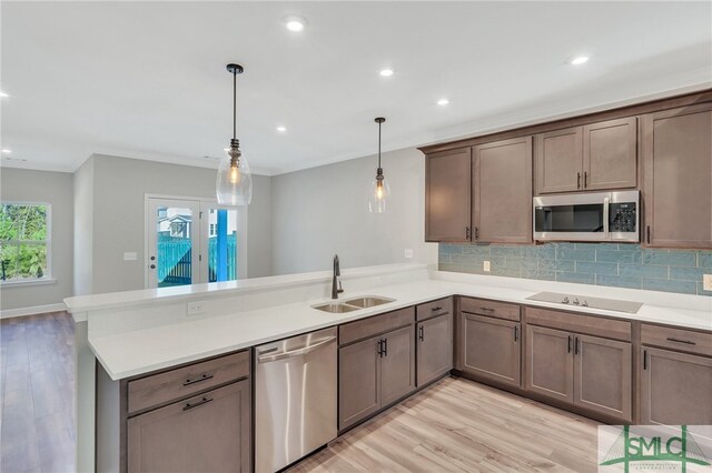 kitchen with appliances with stainless steel finishes, decorative light fixtures, sink, and light wood-type flooring