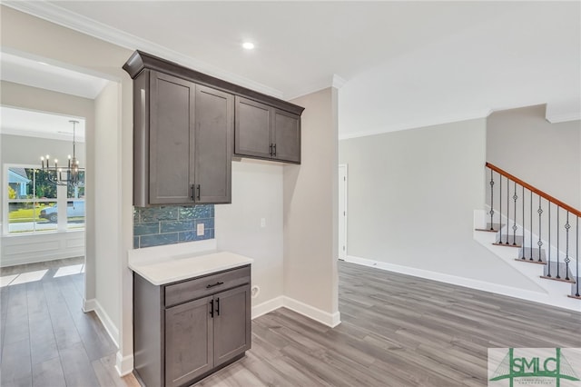 kitchen with light wood-type flooring, backsplash, dark brown cabinetry, crown molding, and an inviting chandelier