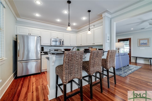 kitchen featuring appliances with stainless steel finishes, white cabinetry, ornamental molding, and hardwood / wood-style flooring