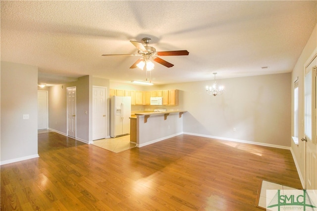 unfurnished living room with a textured ceiling, light wood-type flooring, and ceiling fan with notable chandelier