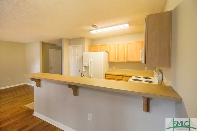 kitchen featuring dark wood-type flooring, a kitchen bar, white appliances, and kitchen peninsula