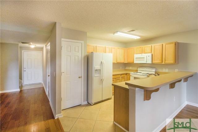 kitchen featuring light tile flooring, a textured ceiling, white appliances, and light brown cabinetry