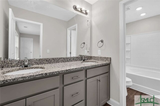 full bathroom featuring double sink vanity, toilet, hardwood / wood-style flooring, and shower / washtub combination