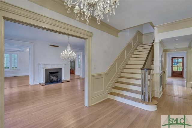 staircase with ornamental molding, a notable chandelier, and wood-type flooring